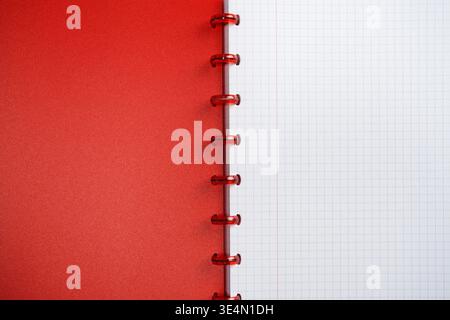Close-up of red spiral notebook with a blank grid page. The notebook has a vibrant red cover and visible red plastic spiral binding. Stock Photo