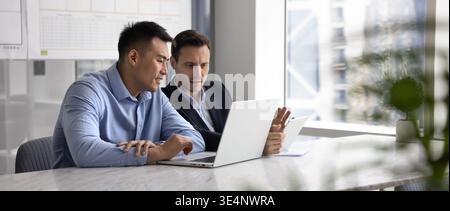 Two diverse male business coworkers compare data on laptop tablet Stock Photo