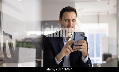 Confident Hispanic business professional using mobile phone at office desk Stock Photo