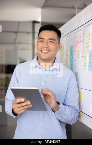 Smiling young entrepreneur standing at planning board holding digital tablet Stock Photo