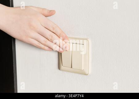 Hand pressing beige light switch on white wall, turning on or off power Stock Photo
