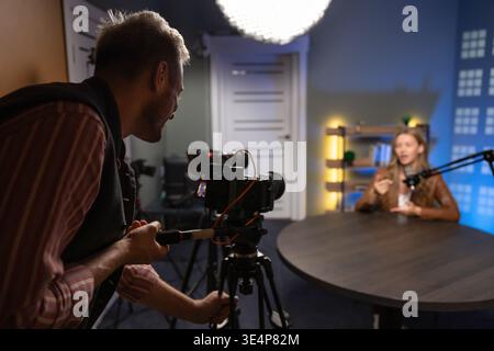 Videographer recording female guest during podcast interview in professional studio Stock Photo