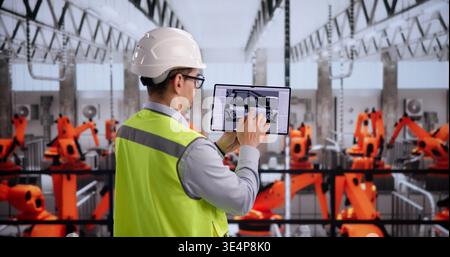 Automotive Technician Reviews Vehicle Components With Tablet In Industrial Plant Stock Photo
