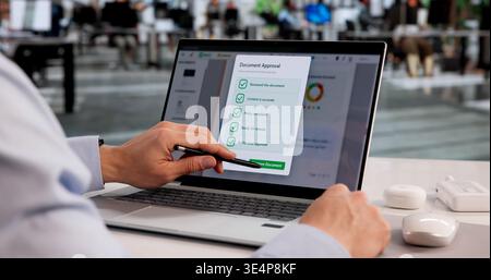 Young Hispanic Male Reviewing And Approving Documents Using Cloud-Based Checklist Software On Laptop Stock Photo