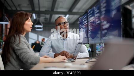 Young Female Coder And Male Software Developer Debug Code On Dual Desktop Monitors Stock Photo