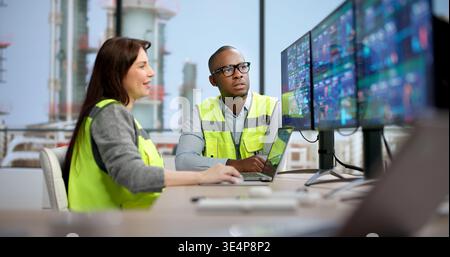 Young Woman And Man Monitor Chemical Plant Production On Multiple Screens, Controlling Industrial Processes Stock Photo