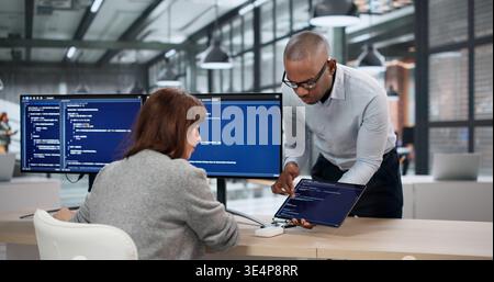 Two Software Developers Coding On Computers As An Accountant Reviews Billing Data Nearby; A Female Engineer Stock Photo