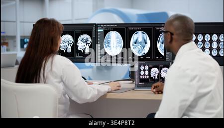 Two Medical Technicians Carefully Study Brain Scans On Computer Screens, Collaborating On Neurological Analysis Stock Photo