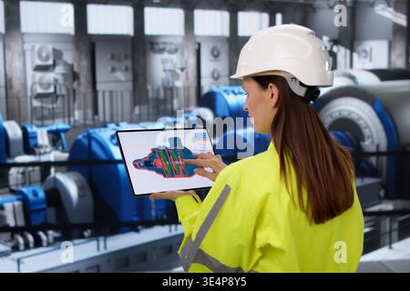 Female Engineer Using Tablet To Monitor Gas Turbine Efficiency At Power Plant Stock Photo