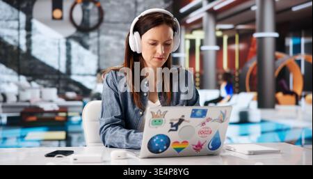 Focused Woman With Headphones Engaged In Online Learning Using Laptop At Modern Workspace Stock Photo