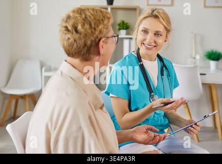 Conversation of smiling nurse and happy elderly patient in modern medical clinic Stock Photo