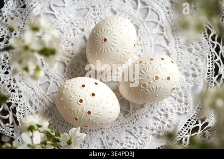 Handmade white Easter eggs decorated with wax and drilled holes, with cherry blossoms in spring Stock Photo