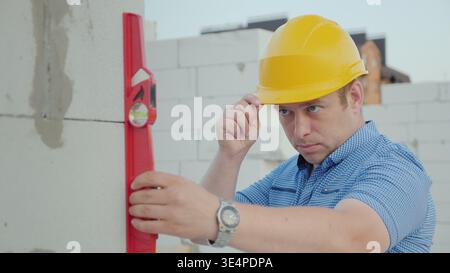 An engineer in a yellow helmet checks the accuracy of the construction work. Quality control at the construction site Stock Photo