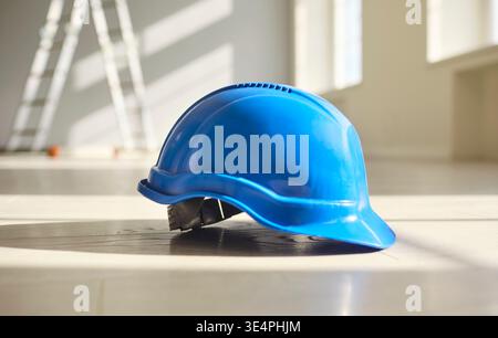 Blue hardhat on interior floor with sunlight, symbol of construction safety Stock Photo