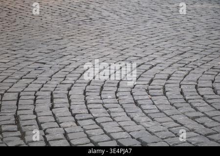 High-angle textured view of a historic cobblestone street featuring gray granite paving stones arranged in a traditional curved fan pattern Stock Photo