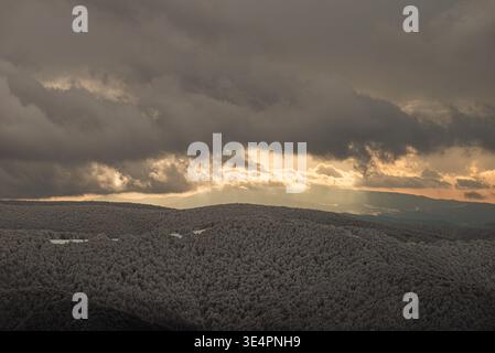Epic winter landscape of the Bieszczady Mountains in Poland, featuring sunbeams breaking through dark storm clouds over snow-covered hills and forests Stock Photo