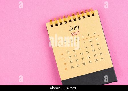 Brown desk calendar for July 2027 on pink background. Stock Photo