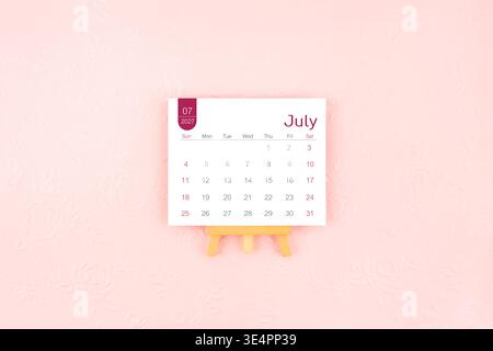 July 2027 calendar page with wooden easel on pink color background. Stock Photo