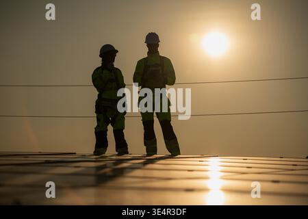 Male and female engineers inspecting solar panel installation points on a rooftop under sunlight, representing clean energy and sustainable development || Model released Stock Photo