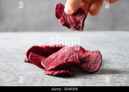 Take a piece vegetable beetroot chips on a gray background. Vegan snack. Close up. Stock Photo