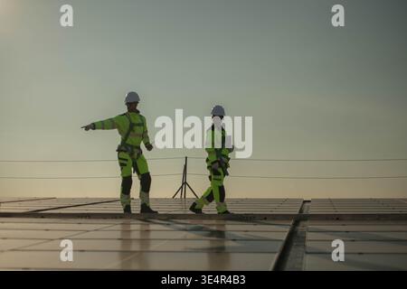 Male and female engineers inspecting solar panel installation points on a rooftop under sunlight, representing clean energy and sustainable development || Model released Stock Photo