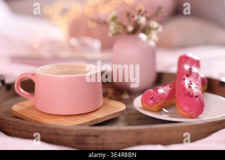 Aromatic coffee in cup, eclairs, and beautiful flowers on bed, closeup Stock Photo