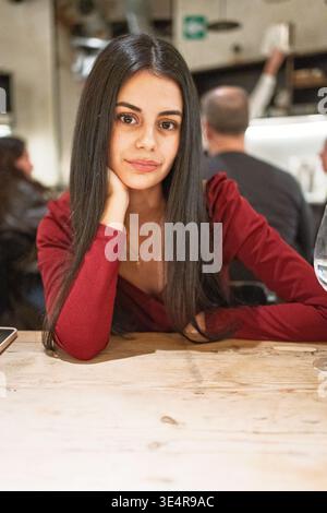 Young woman with long dark hair, wearing a red top and resting chin on hand Stock Photo