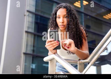 Youthful African American female individual engages with her mobile device high above city streets Stock Photo