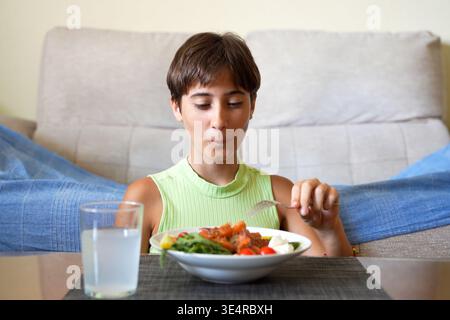 Child reviews meal. Child examining fork thoughtfully. Child ponders over salad with water cup Stock Photo
