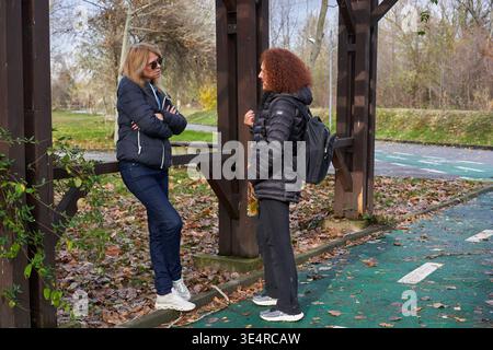 Two middle aged women friends laughing and talking animatedly in an autumn park Stock Photo