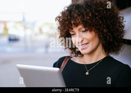 Female entrepreneur with curly hair smiling and managing orders outdoors in bright natural sunlight Stock Photo