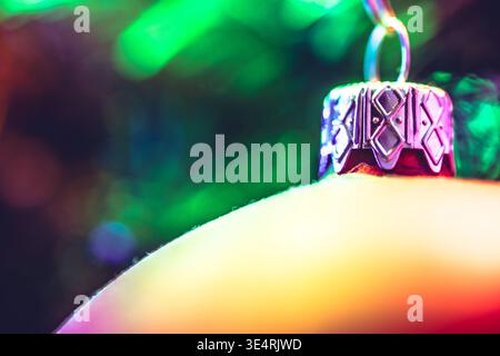 Closeup of a colorful Christmas ornament with a silver patterned cap against a blurred green and dark background. Stock Photo