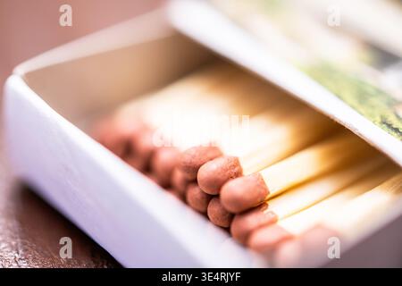 Close-up of an open paper matchbox showing several wooden matchsticks with pink tips inside on a blurred warm-toned surface. Stock Photo