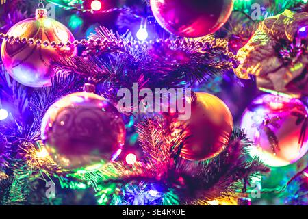 Close-up of shiny baubles and tinsel on a Christmas tree with multicolored lights in a festive indoor decoration scene. Stock Photo