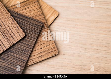 Overlapping rectangular wood veneer sample swatches in different grain patterns lie on a light wooden surface with copy space on the right. Stock Photo