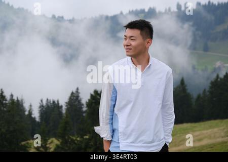 smiling Asian male tourist looking away against the scenic foggy forest background of Mount Rigi, Switzerland. Stock Photo