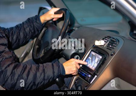 Driver navigating in car using a touch screen display on the dashboard while holding the steering wheel, highlighting modern driving challenges and po Stock Photo