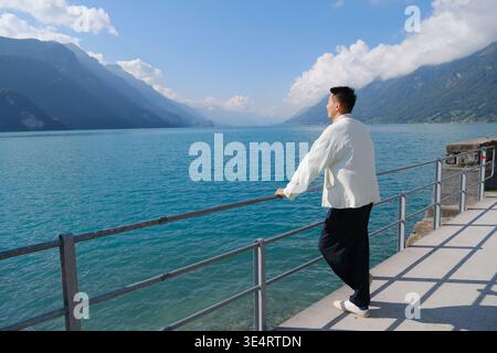 man leaning on a railing and gazing at the turquoise Lake Brienz in Switzerland Stock Photo