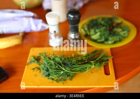 Fresh dill on cutting board with spices and salad in background, healthy cooking and organic food concept. Stock Photo