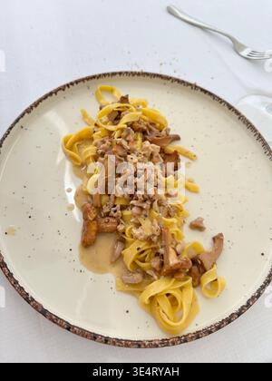 Delicious homemade tagliatelle pasta with forest chanterelle mushrooms in a creamy sauce. Gourmet Italian lunch served on a white tablecloth. Food. Stock Photo
