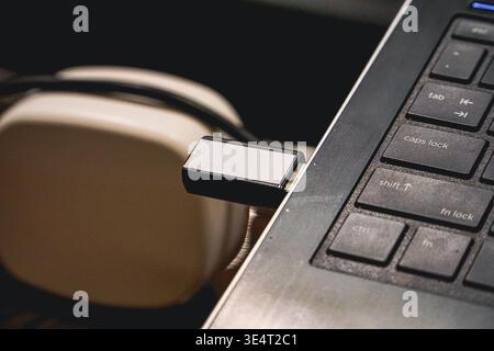 USB flash drive plugged into a laptop beside over-ear headphones, representing data transfer, storage, and digital work setup. Stock Photo
