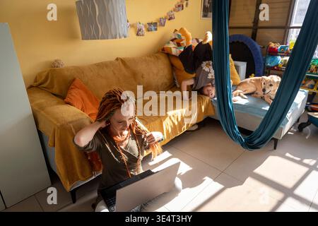 Wide angle shot of woman with laptop on floor and boy doing handstand on sofa in living room. Stock Photo