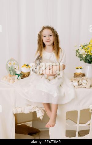 Adorable girl holding bunny in soft Easter decor, bright minimal studio portrait with spring mood Stock Photo