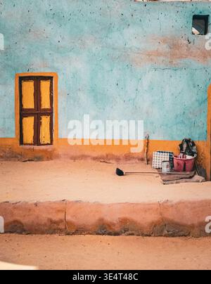 Traditional nubian house facade with vibrant blue and orange walls, featuring a small yellow window and daily life objects in rural Egypt. Stock Photo