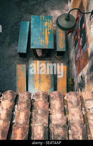 High-angle view of rustic blue and yellow tables by a stone wall with a mural and terracotta tiles. Stock Photo