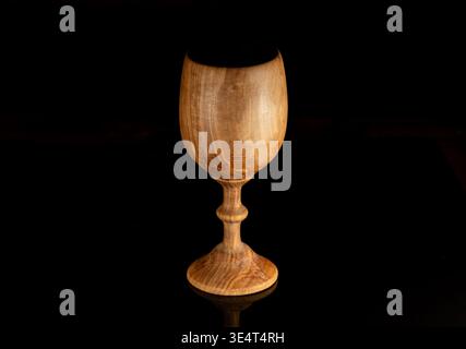 Wooden goblet photographed on a black background in dramatic light. Minimal still life image with natural wood texture, elegant shape and copy space. Stock Photo