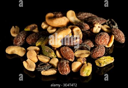 Close-up of mixed nuts and dried fruits scattered on a black background. Healthy snack concept, natural food, copy space. Stock Photo