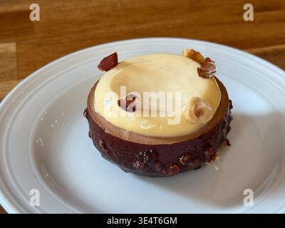 Hazelnut dessert pastry with glossy cream topping served on a white plate in close view. Gourmet patisserie presentation, menu styling and indulgent Stock Photo