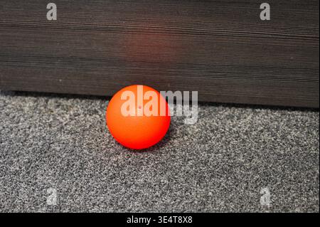 Single bright orange ball with a small hole rests on a textured gray carpet Stock Photo