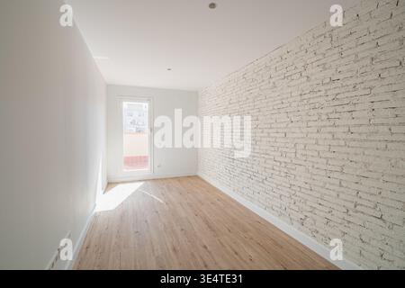 Empty room with white brick wall and wooden floor. Natural light enters through the door, creating a bright and spacious atmosphere. Stock Photo